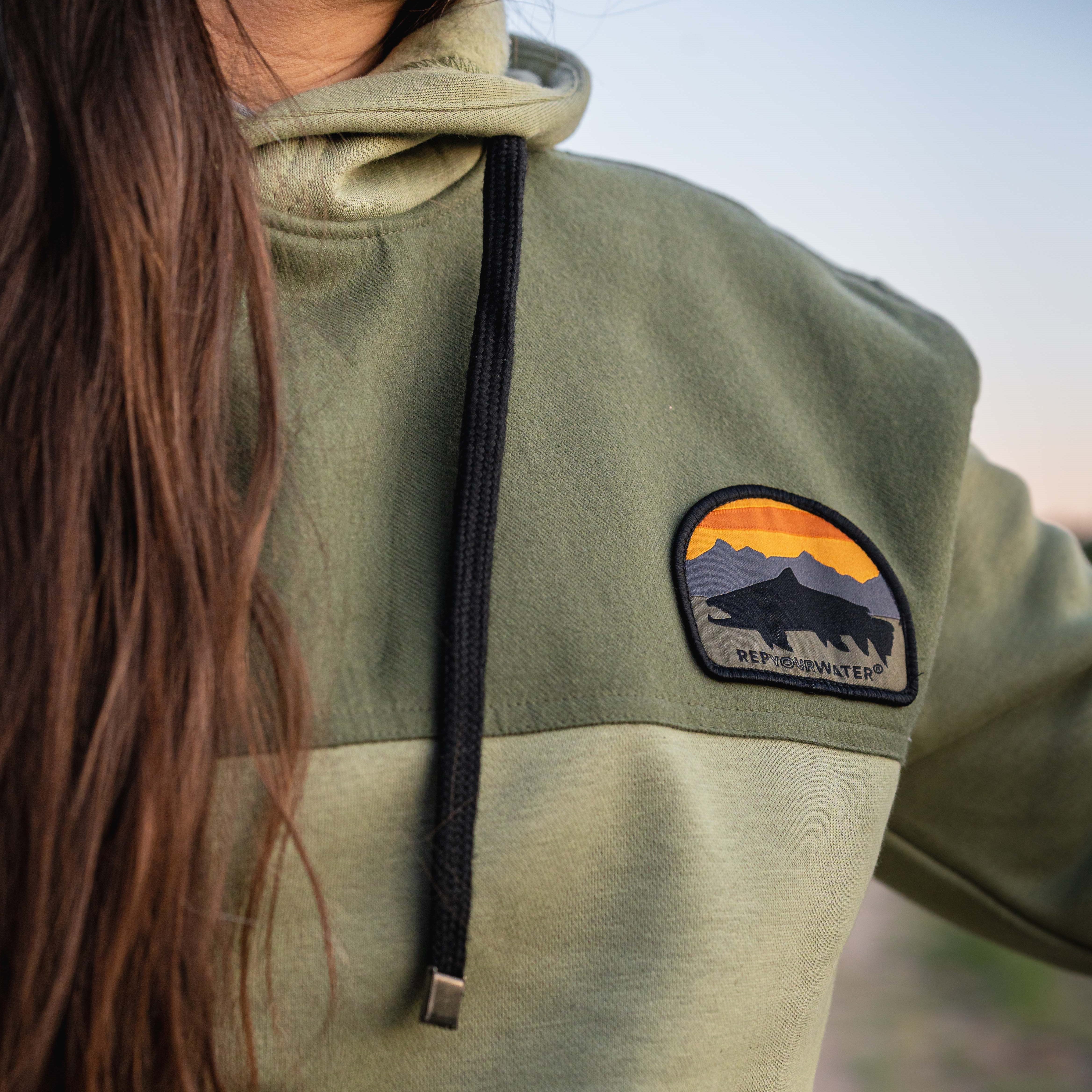 close up photo of the green hoodie with a patch and a fish in black