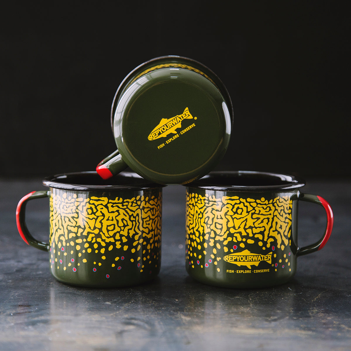 Three mugs are shown. The bottom two show the sides which have a brook trout skin print. The one on top of the other two show the bottom which has a logo which reads repyourwater inside a trout silhouette and fish explore conserve underneath