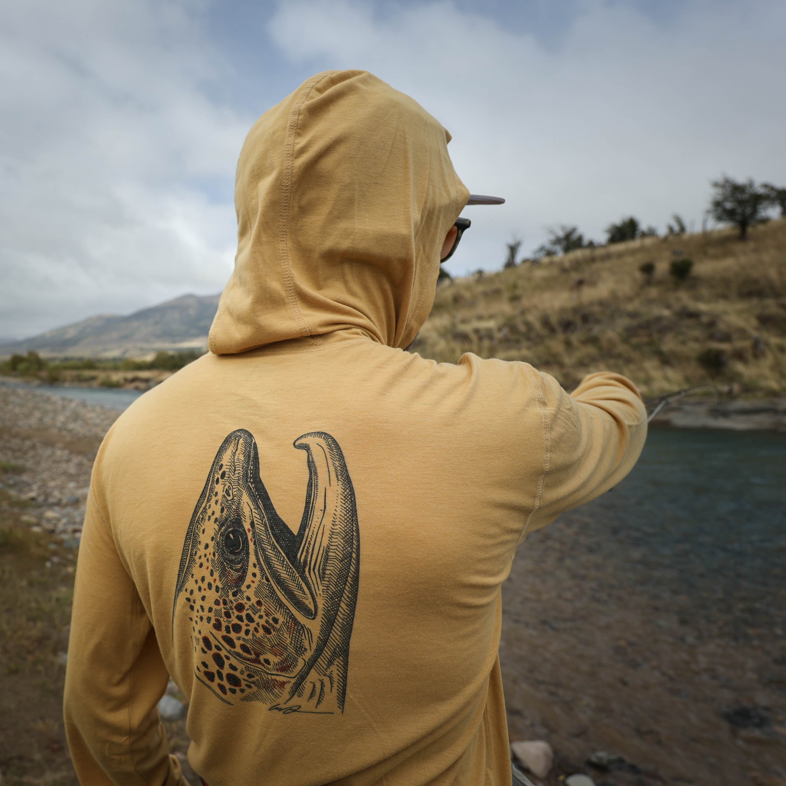 man wearing dark tan sun hoody with a brown trout head on the back on the buckskin merino breeze sun hoody by repyourwater