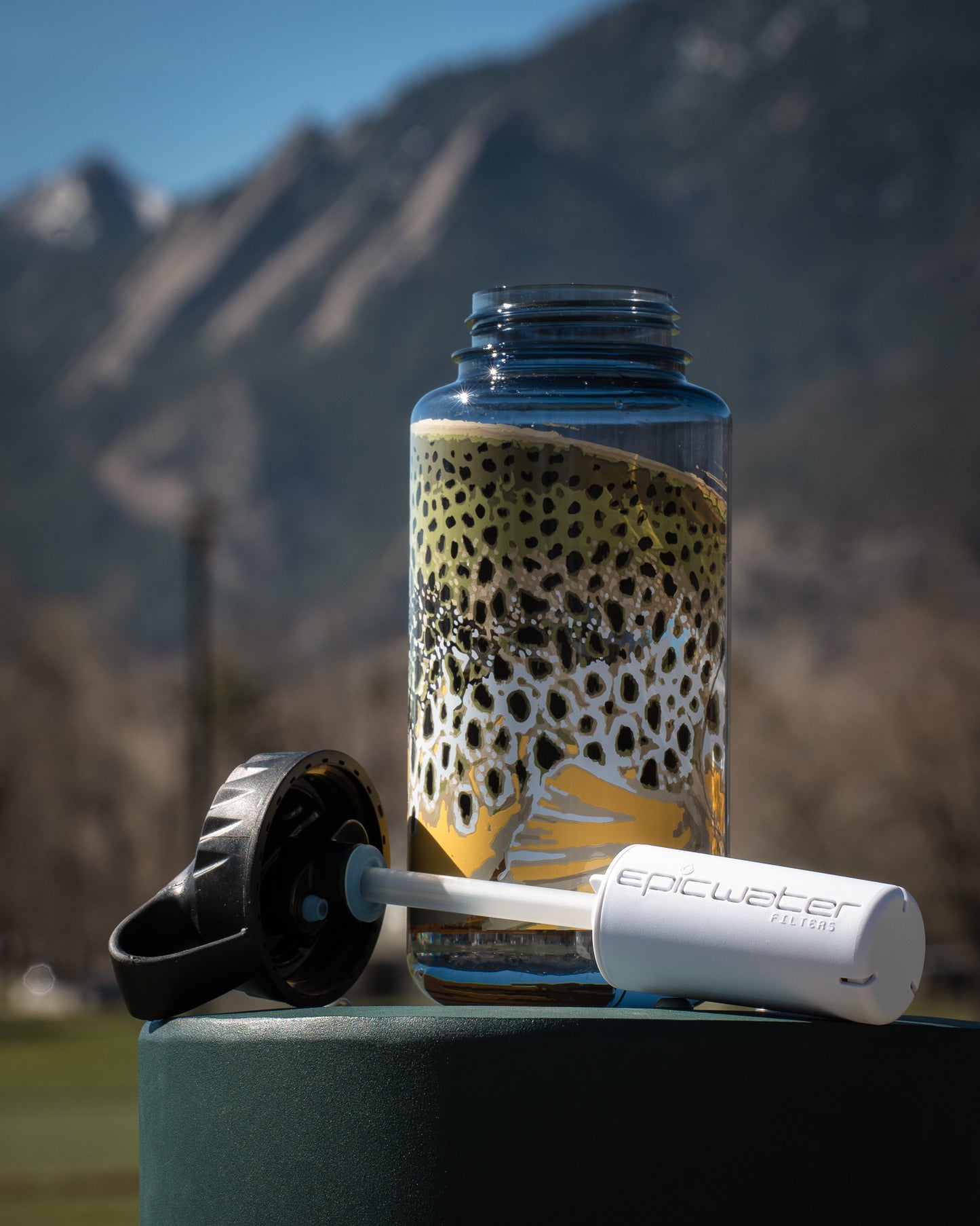 Plastic water bottle featuring a brown trout design showcasing the Epic everywhere filter system in front of a mountain background.