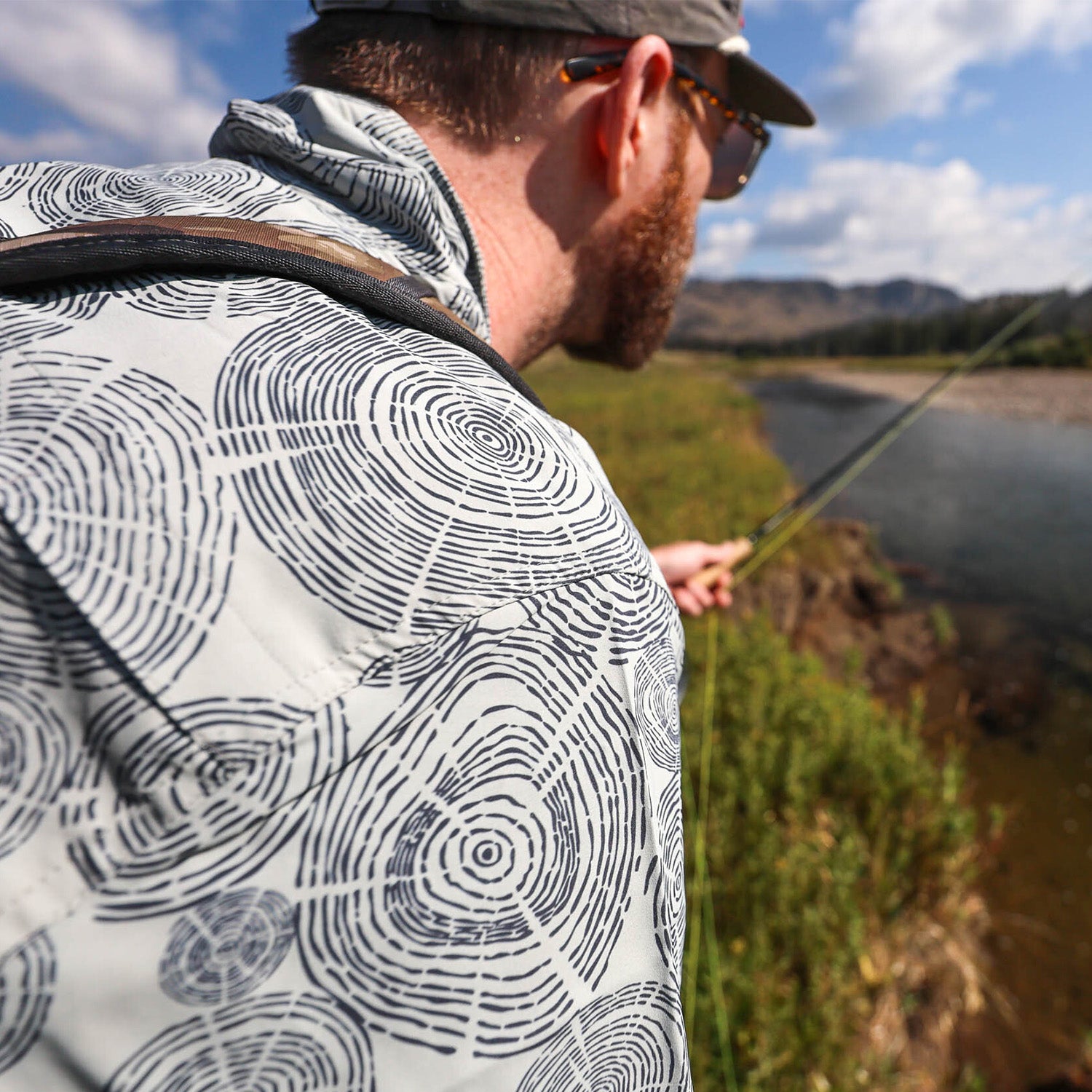 man fishing on a river wearing a tree ring pattern deschutes button down shirt