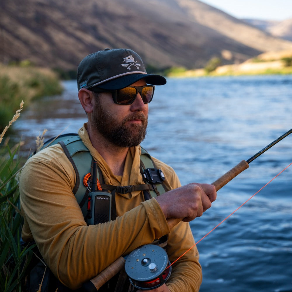 Man fishing by a river with mountains in the background