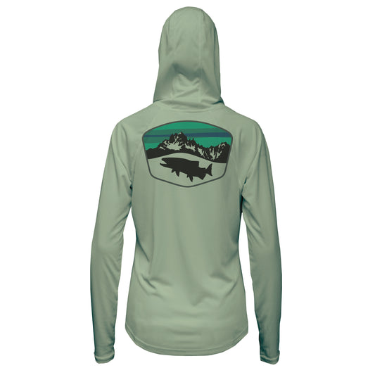 A light green hooded shirt with a black trout underneath a mountain scene with a green and blue sky pattern within a badge shape