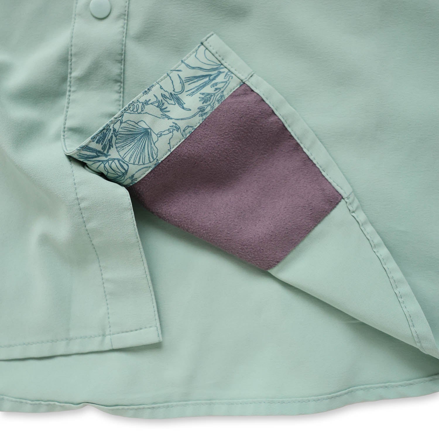 Close-up of a light green/cenote button down shirt with a sea floor doodle lining and sunglass wipe on a white background