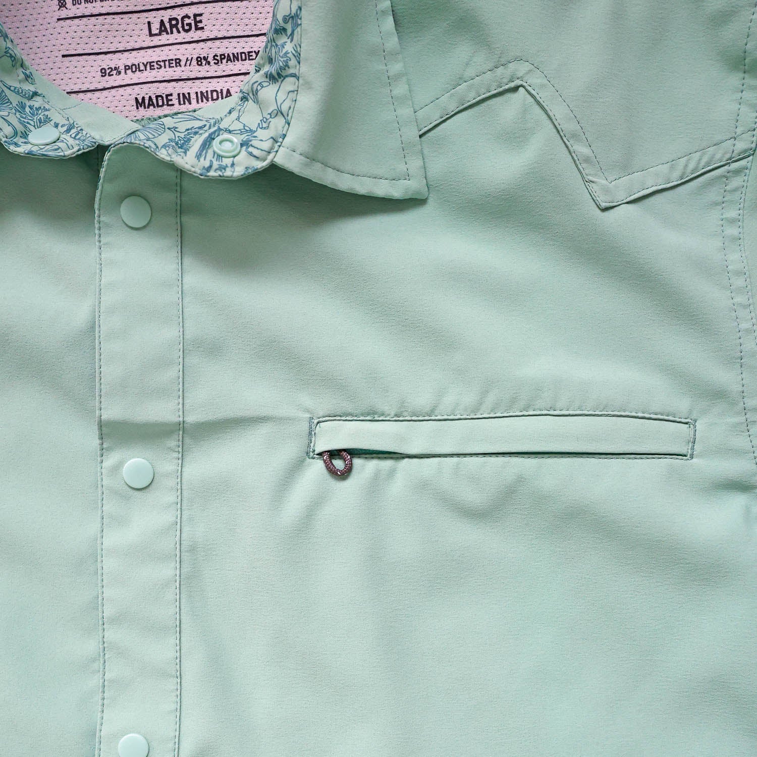 Close-up of a light green/cenote button down shirt with a sea floor doodle lining collar and chest pocket