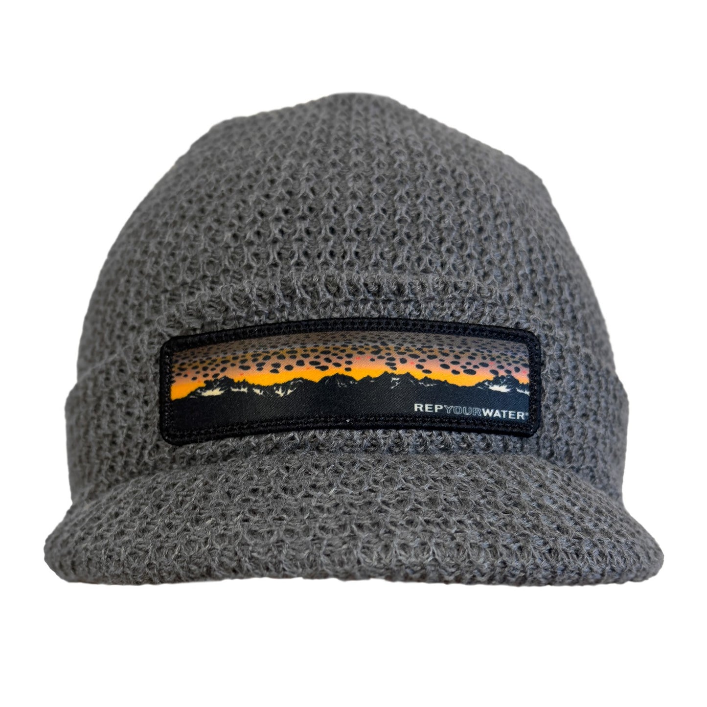 Light gray knit hat with a brim and a patch on the front showing a mountain range and brown trout skin as the