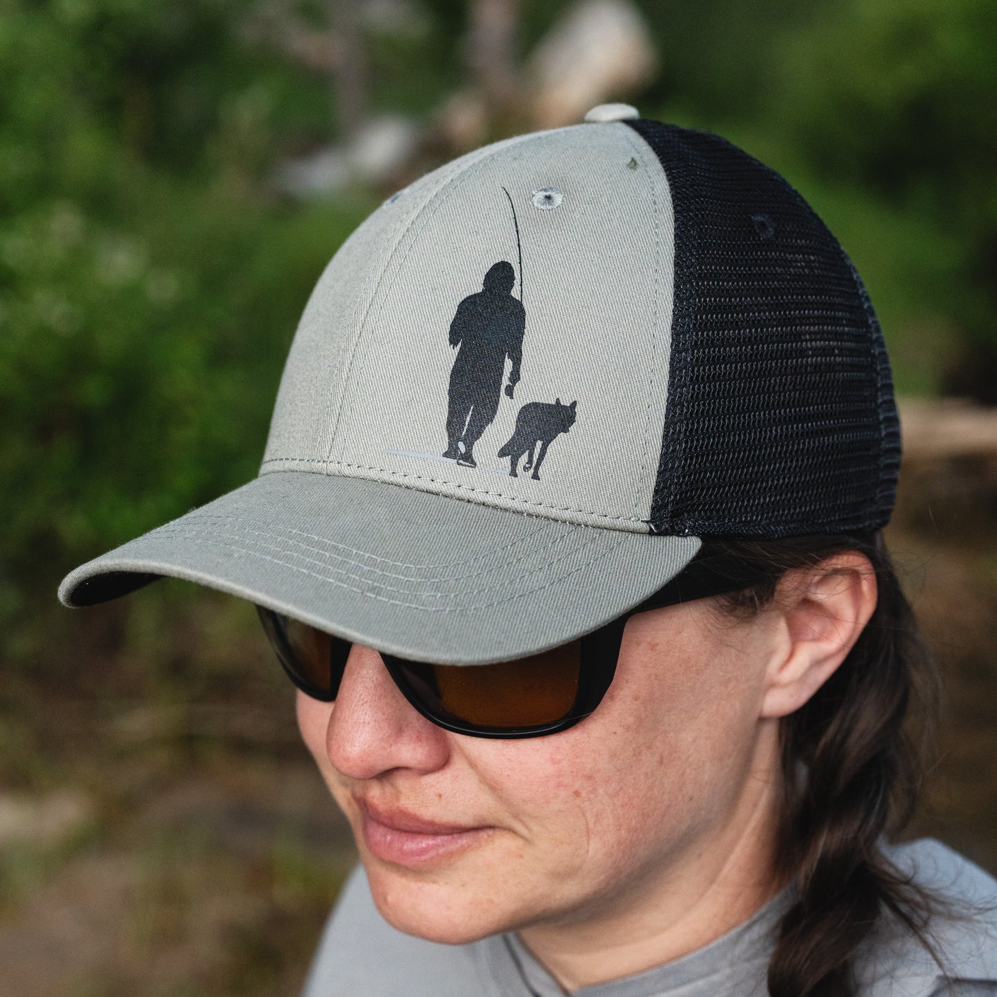 woman wearing a green hat with black mesh and dog/wolf back with a squatch silhouette on the front