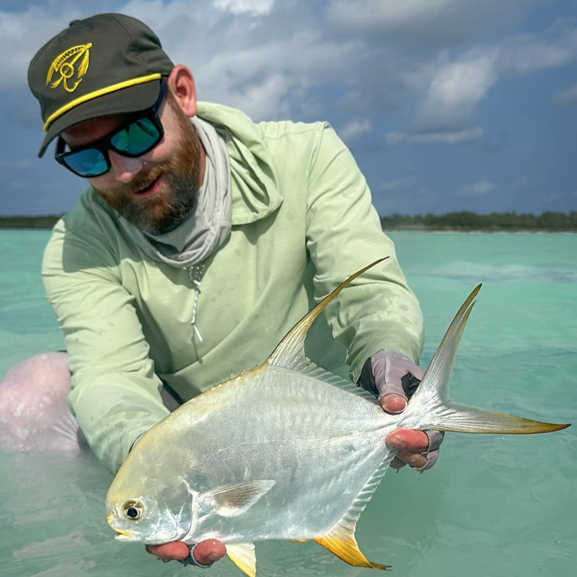 man holding a permit with the infamous string duster collab hat on with banjo fly design and unstructured five panel fit