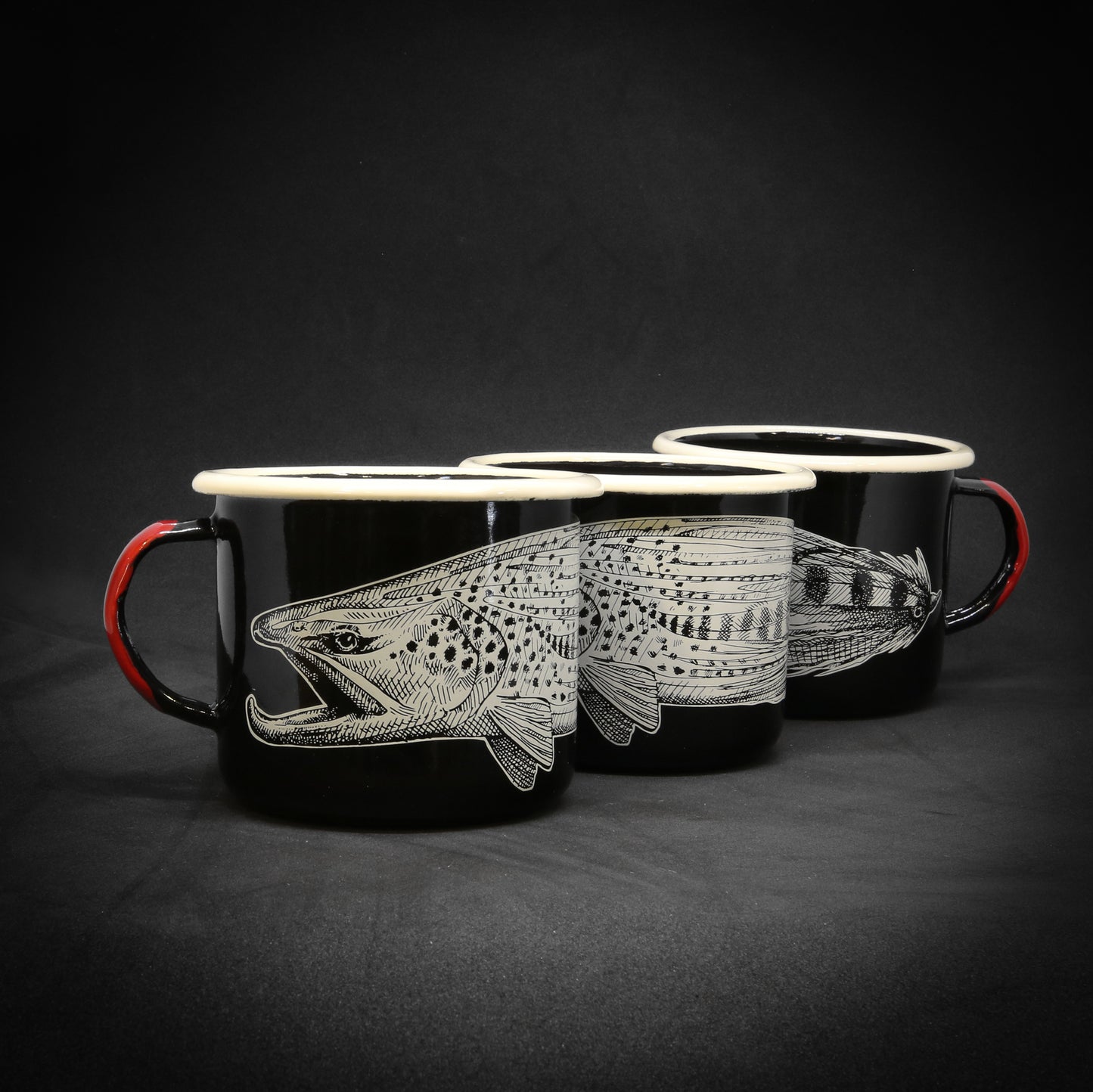 three black mugs staggered to show the full design of a brown trout head and the front half of a streamer in black and white