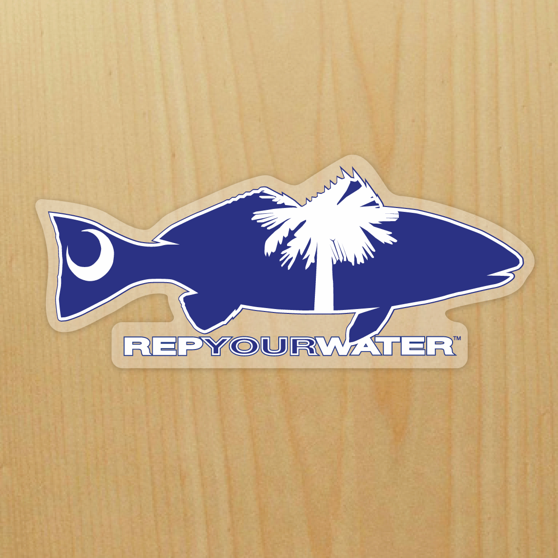 A sticker on a wood background features a redfishwith a palm tree and moon inside above the words repyourwater