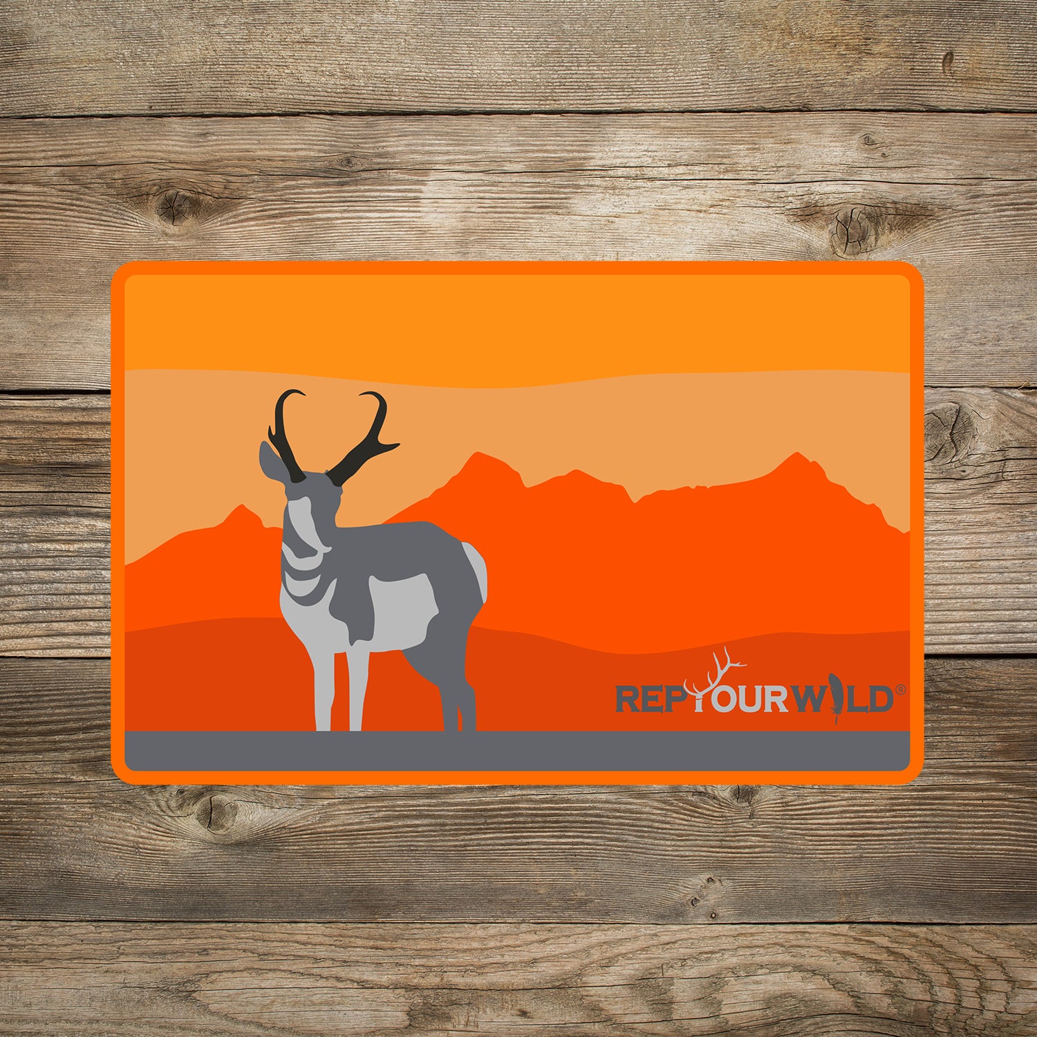 A sticker on wood background features an antelope in front of mountains in a rectangular shape