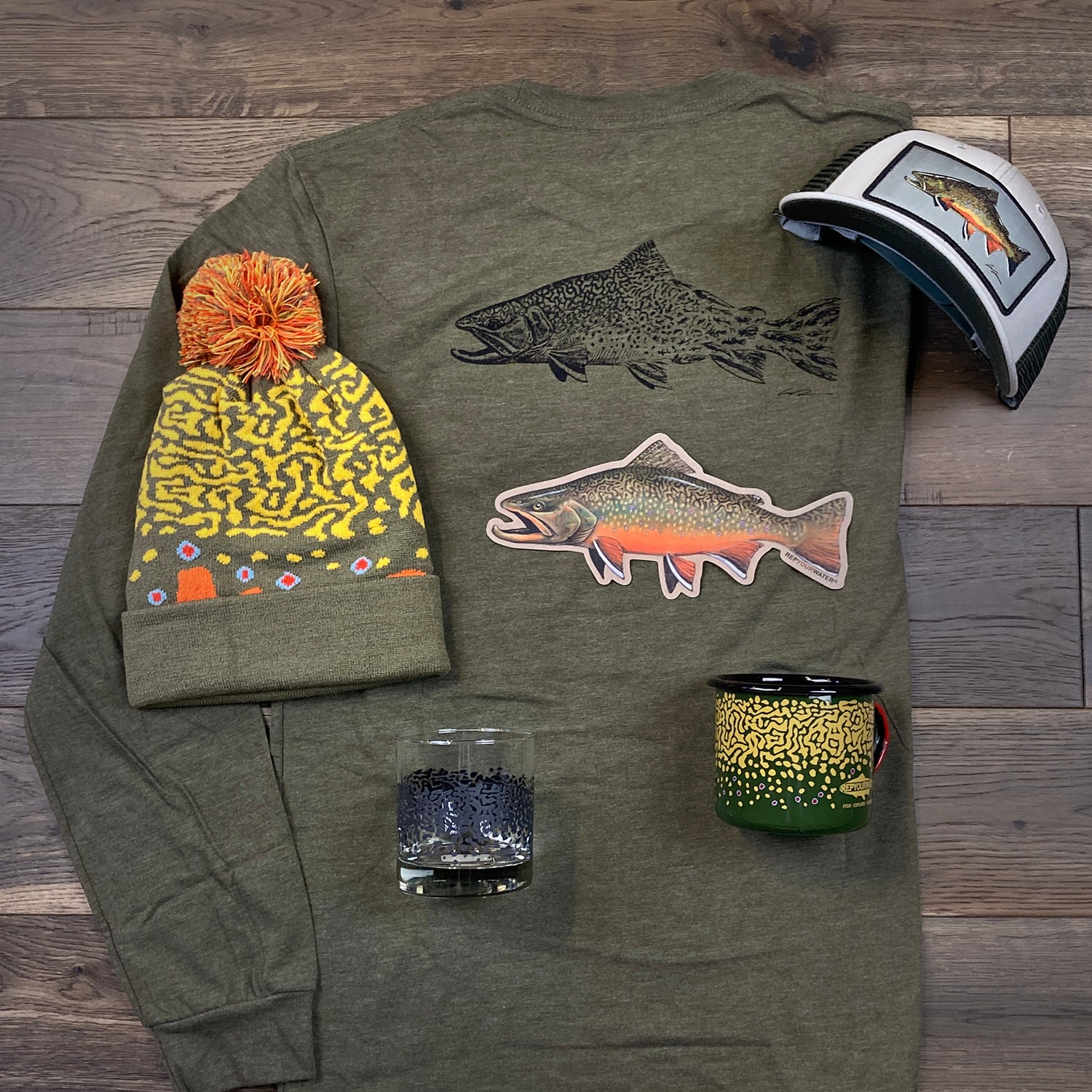 A long sleeved shirt, knit hat, sticker, mug, glass and brimmed hat A hat, shirt, pair of socks and two stickers laid out on a wood floor.