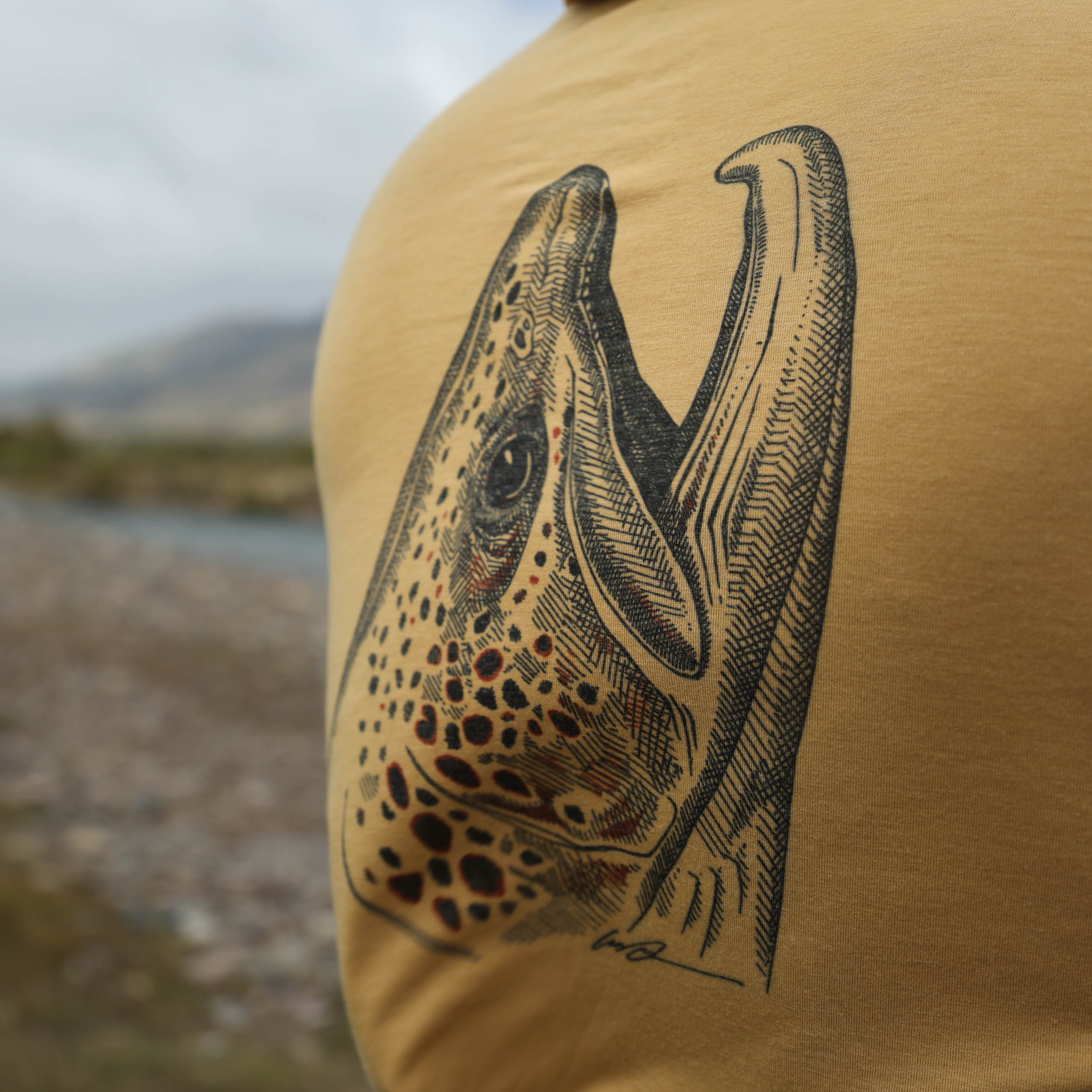 dark tan sun hoody with a brown trout head on the back on the buckskin merino breeze sun hoody by repyourwater close up