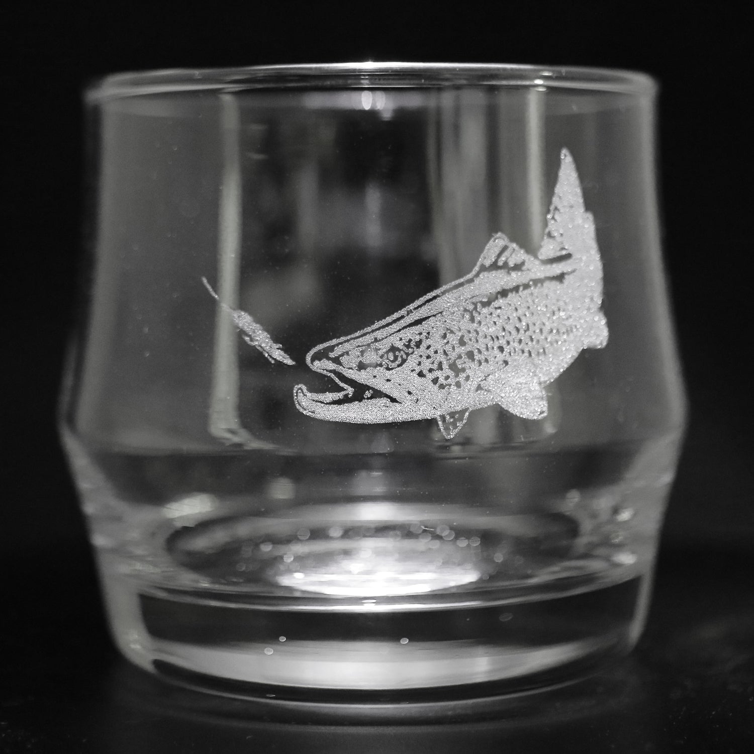 a lowball style glass with an etched trout chasing a fly on it