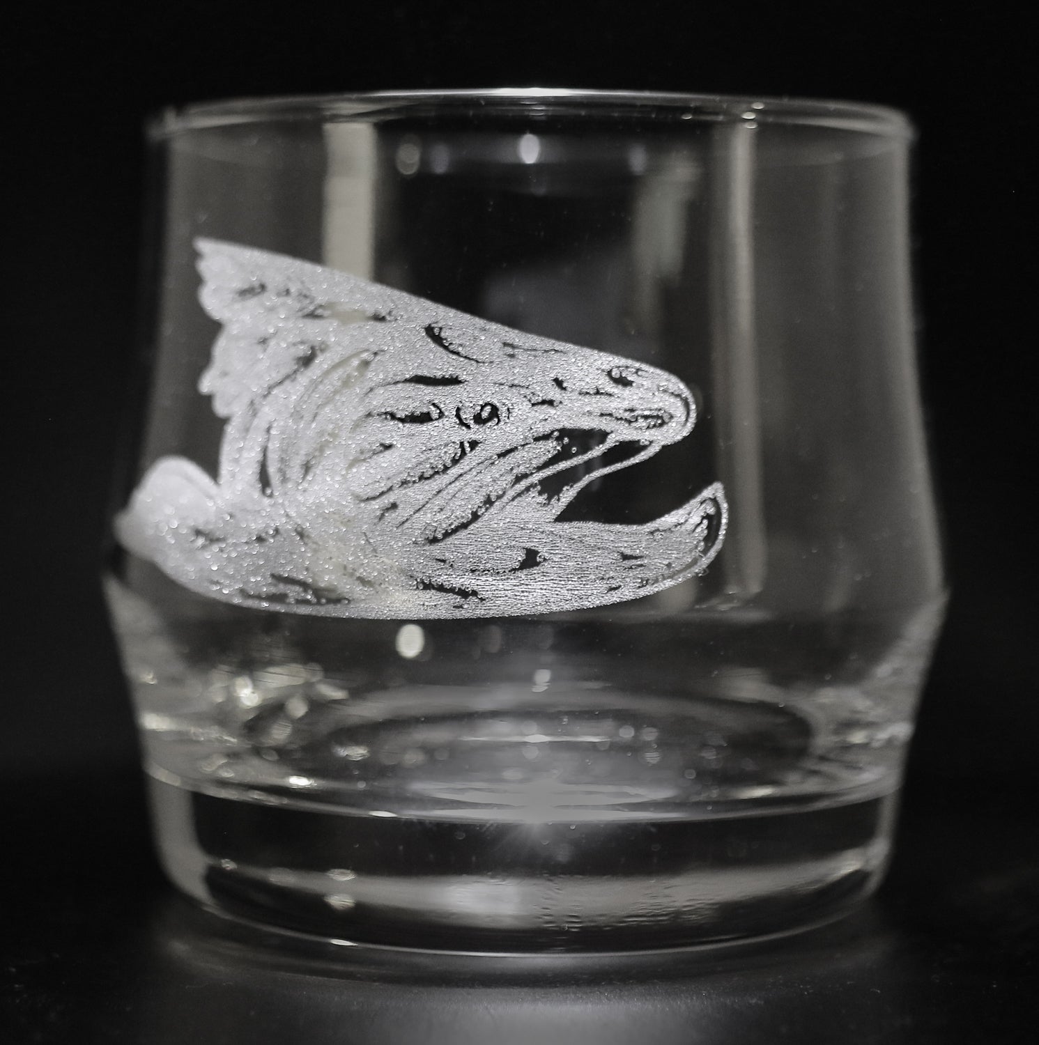A rocks glass with a fish head made of flies etched into the side