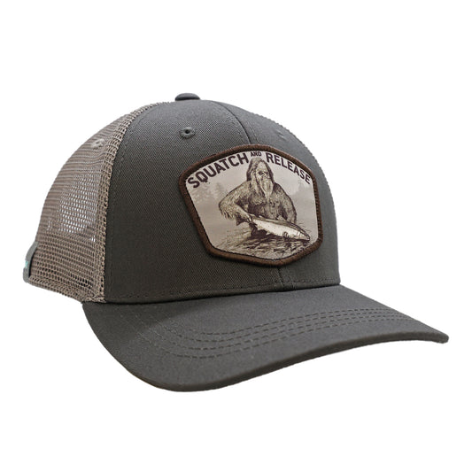 A hat with white mesh back and gray front. The front features a design with sasquatch releasing a fish with mountains that says squatch and release.