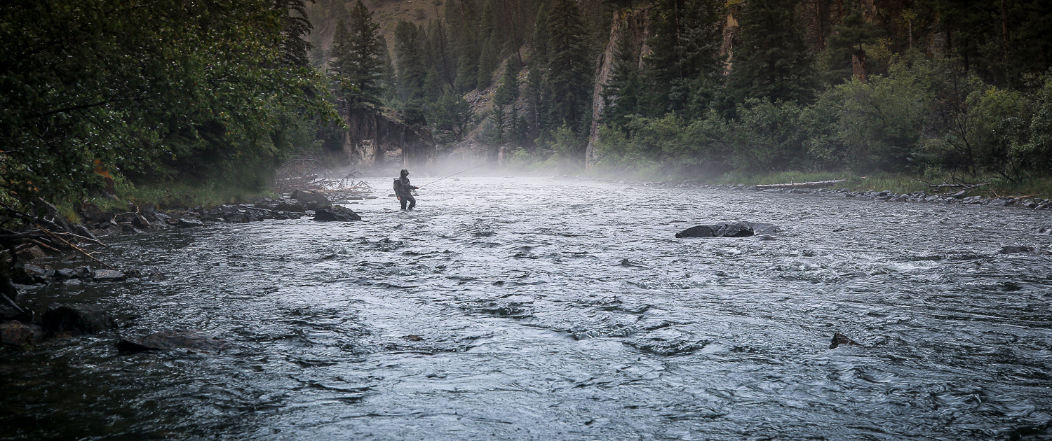 An angler walking in a river with mist