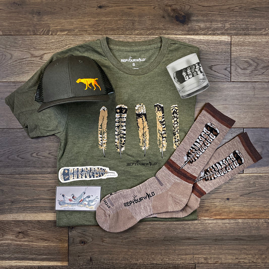 A hat, shirt, pair of socks, glass and two stickers laid out on a wood floor.