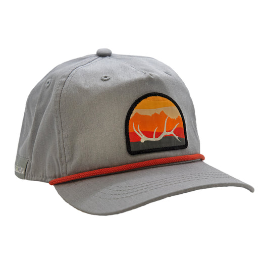 gray full cloth hat with a black rope. on the front a half circle patch that shows a sunset, mountain range, and a white elk antler