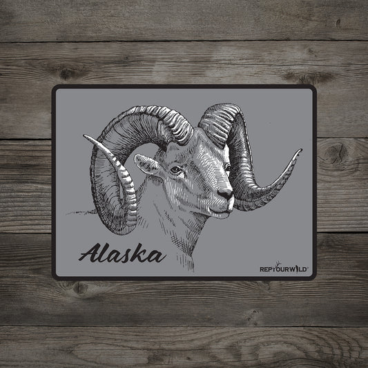 A sticker on a wood background with a dall sheep on it and reads alaska repyourwild