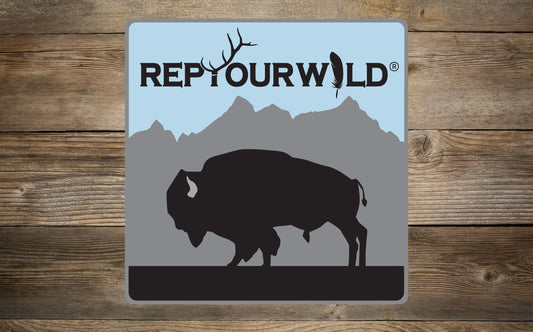 A wood background with a mockup of a sticker showing a bison silhouette a mountain range and the words rep your wild