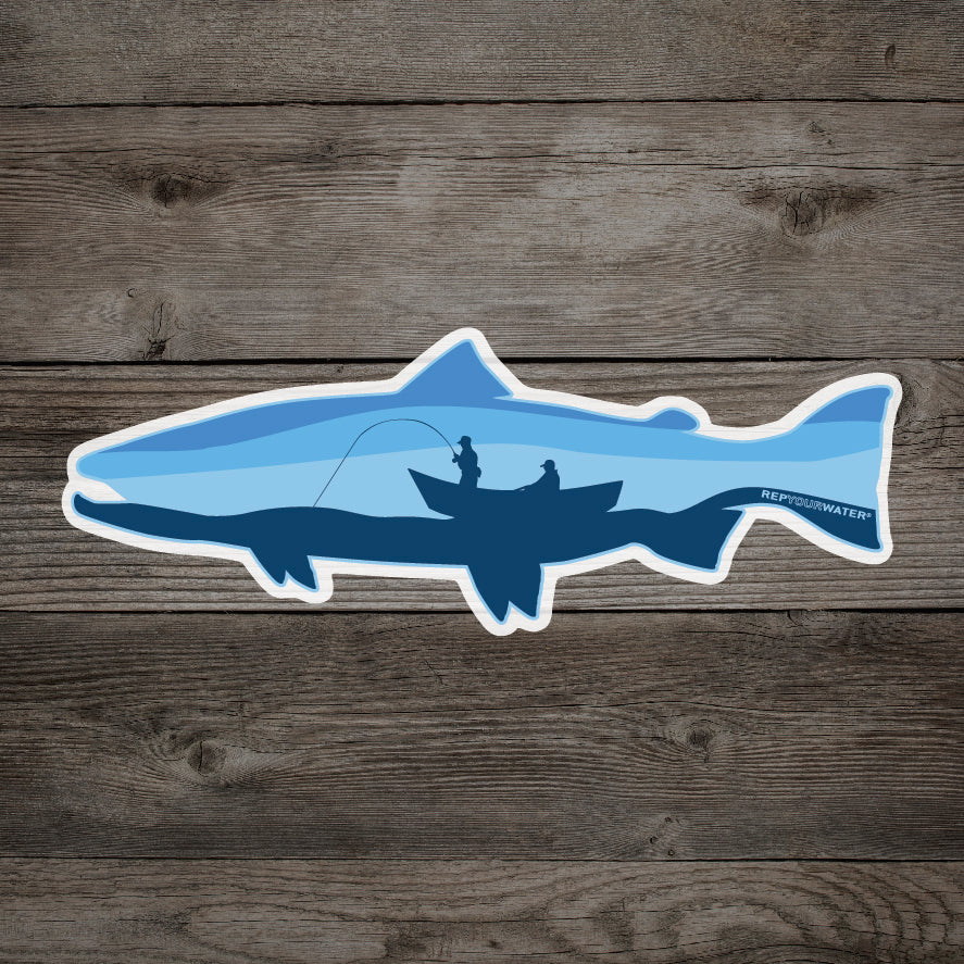 A wood background has a mockup of a sticker of a trout with a drift boat and angler inside