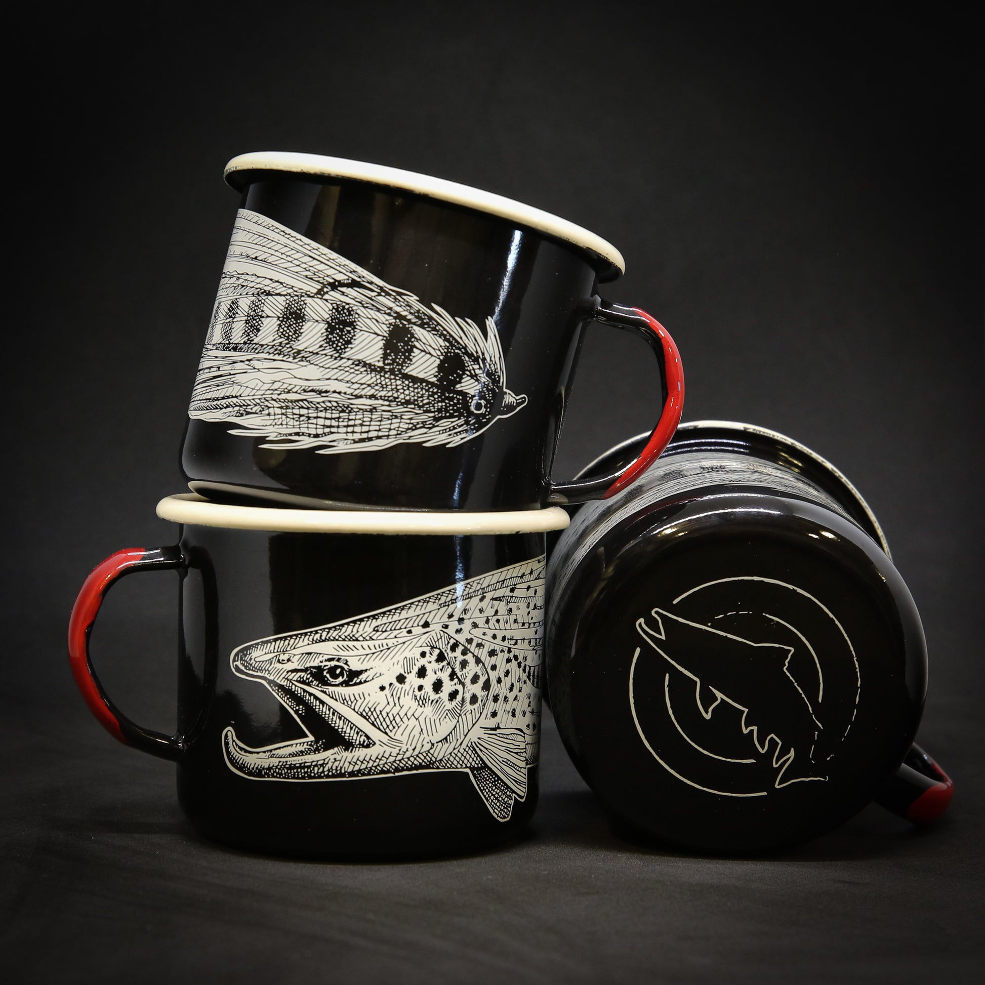 Three black mugs that shows a brown trout head connecting to the front half of a streamer in black and white. the bottom of the mug shows a trout silhouette inside two circles