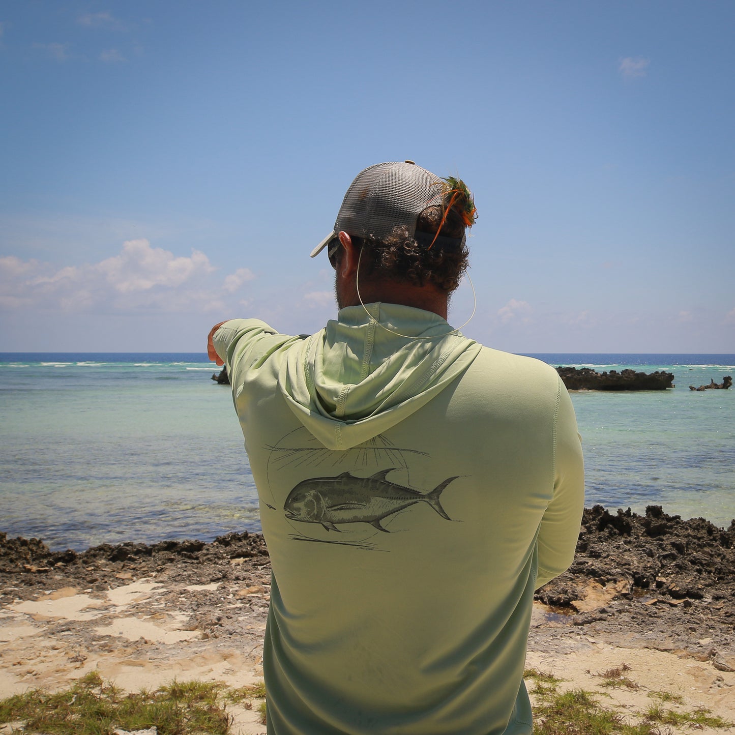 a fly fishing guide points towards the ocean while wearing a green shirt featuring a giant trevally 