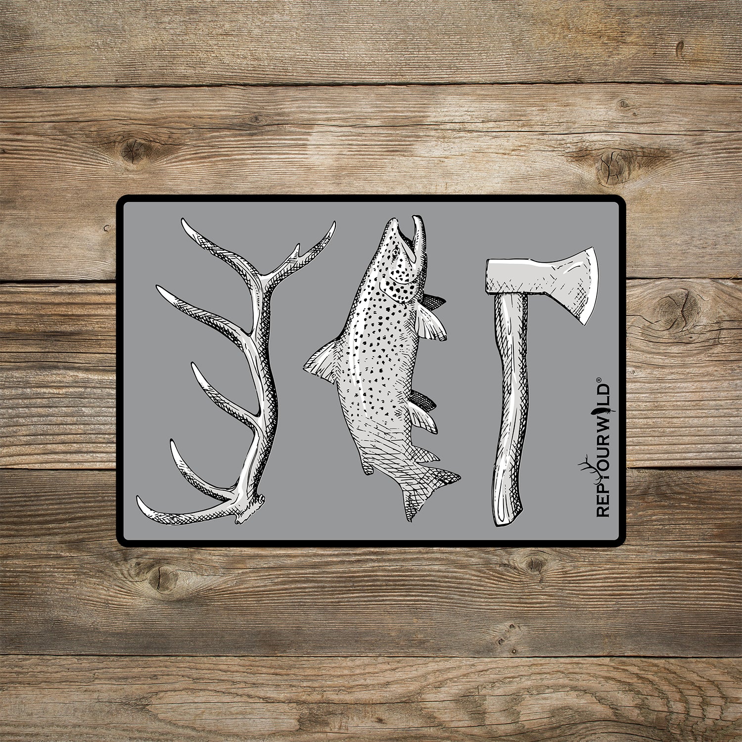 A gray rectangular sticker shown on a wood background. The sticker features an elk antler, a trout and a hatchet.
