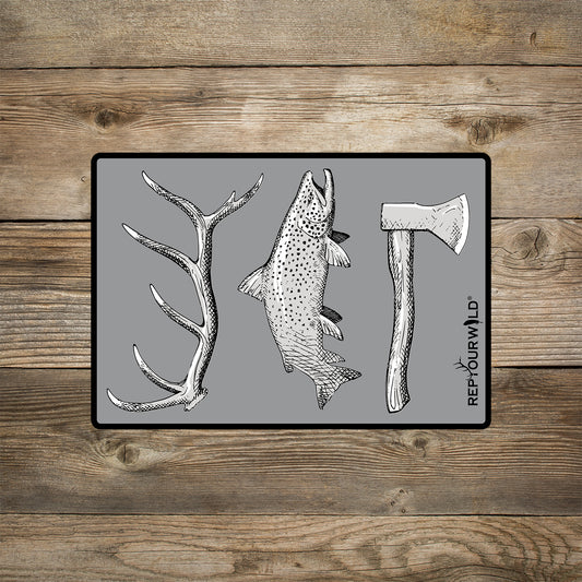 A gray rectangular sticker shown on a wood background. The sticker features an elk antler, a trout and a hatchet.