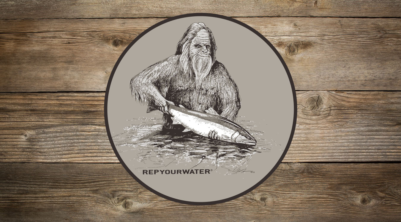 A sticker on a wooden background features drawing of a sasquatch holding a fish in the water