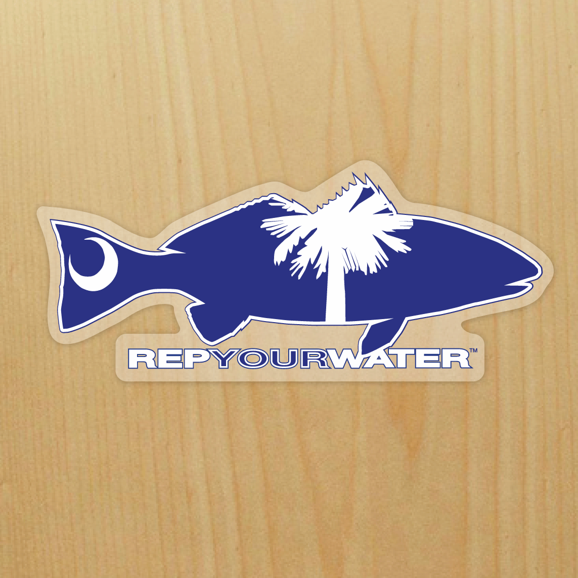 A sticker on a wood background  features a redfishwith a palm tree and moon inside above the words repyourwater