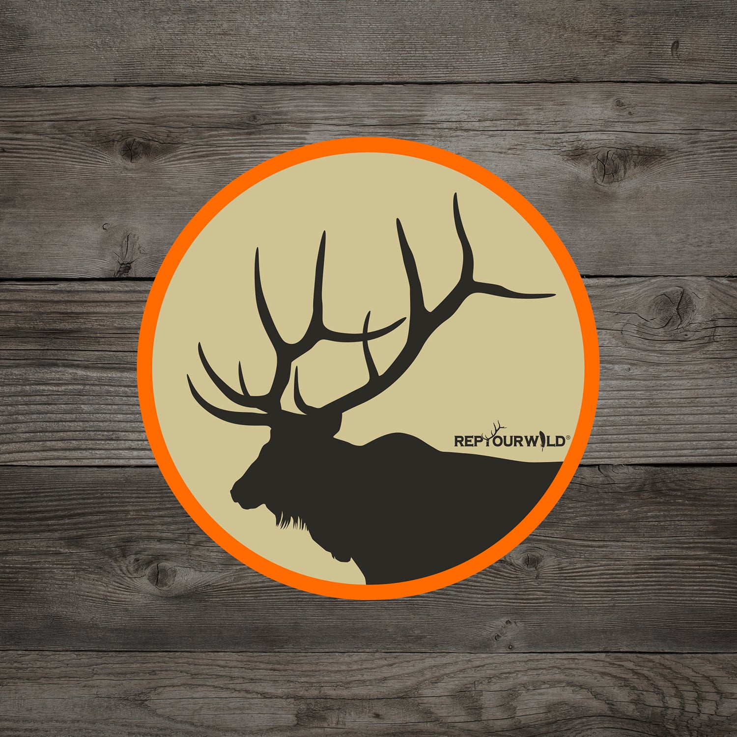 A sticker on a woodbackground has an elk head and antlers inside a circle with the word repyourwild