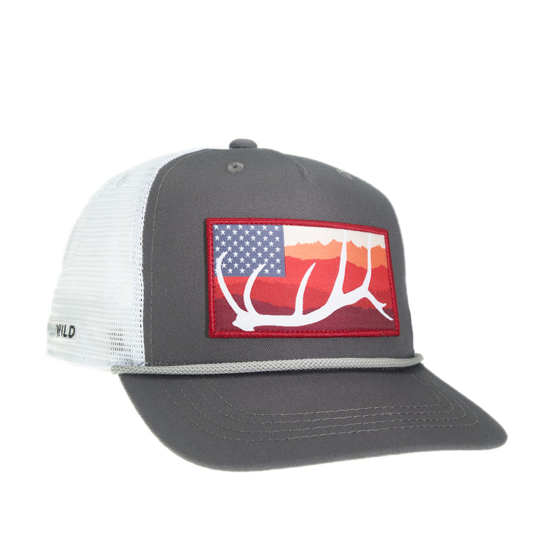 A hat with white mesh and gray fabric has a patch with an elk antler in front of mountains and 50 stars in a blue rectangle with a white rope above the brim